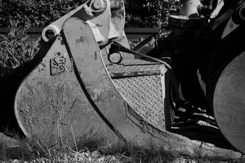 Monochrome image of an excavator bucket in a construction site.